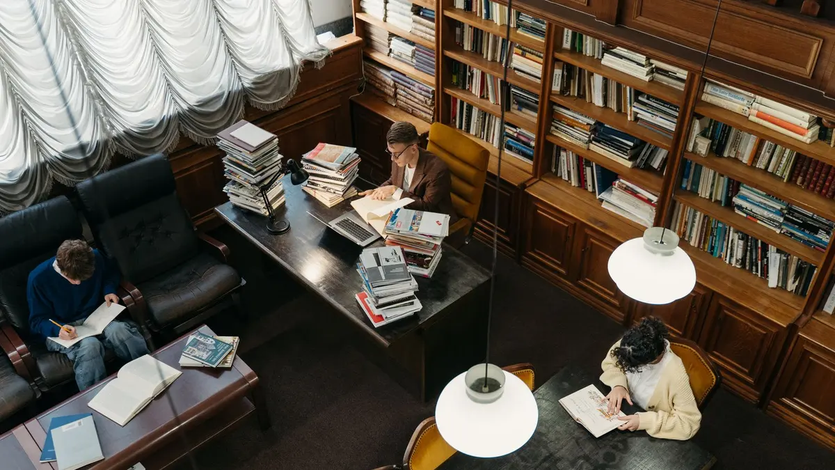 Students studying among bookshelves in a wood-panelled university library reading room