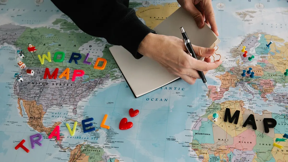Hands planning a trip on a world map with travel pins, comparing Australia and New Zealand as study destinations