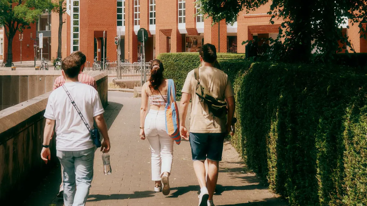 University students walking along a tree-lined campus pathway toward a brick university building